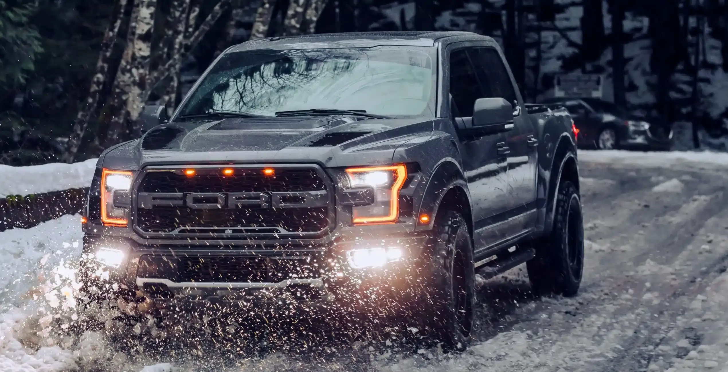 Gas vehicle repair in Palmer, AK at 1023 Diesel & Fleet: a gray pickup truck with its lights on driving through a snowy, muddy forest road.