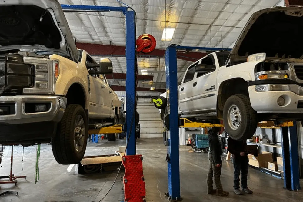 Two diesel pickup trucks on lifts inside the 1023 Diesel & Fleet repair shop.