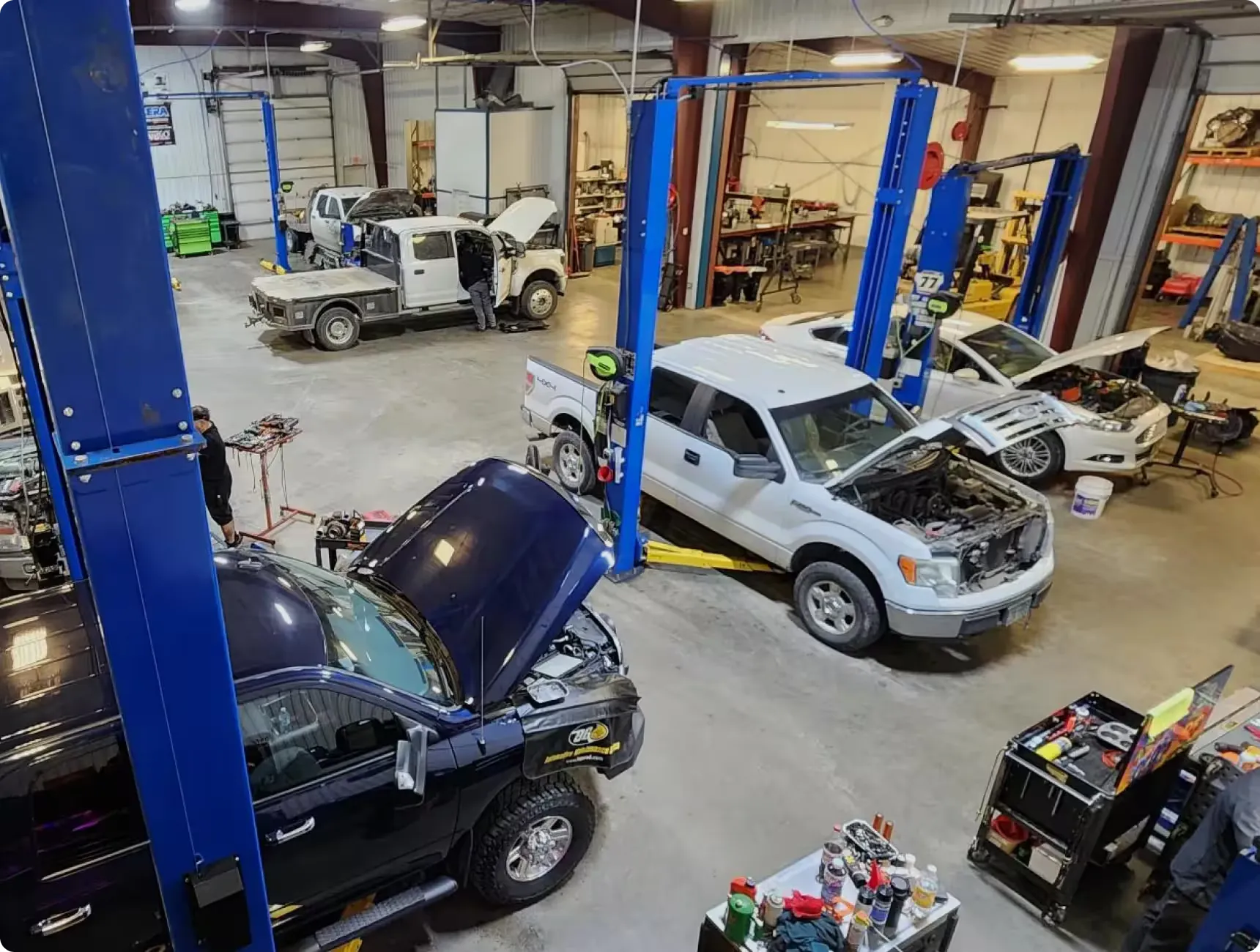 A busy auto repair shop with multiple vehicles being serviced and mechanics working on cars with open hoods.